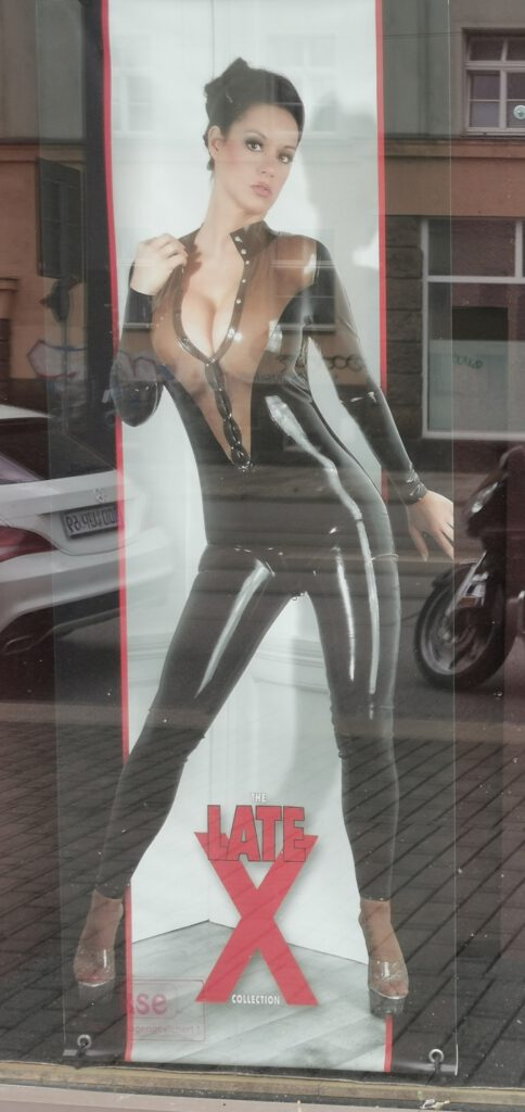 Werbeplakat mit einer Frau in Latexkleidung und dem Text "Late X"