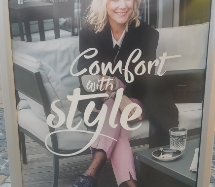 Werbeplakat mit dem Title "Comfort in Style" mit einer blinden Frau auf einer Bank.