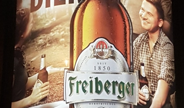 Werbeplakat der Biermarke "Freiberger" mit dem Titel "Bleib wie dein Bier" mit zwei Männern und einer Frau, die Bier trinken.