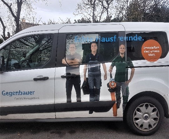Bild eines Werbeaufdrucks auf einem Auto mit drei Männern und dem Titel "Echte Hausfreunde"