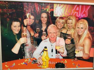 Werbeplakat der Bar "Klax" mit einem Mann in der Mitte und vielen Frauen um ihn herum