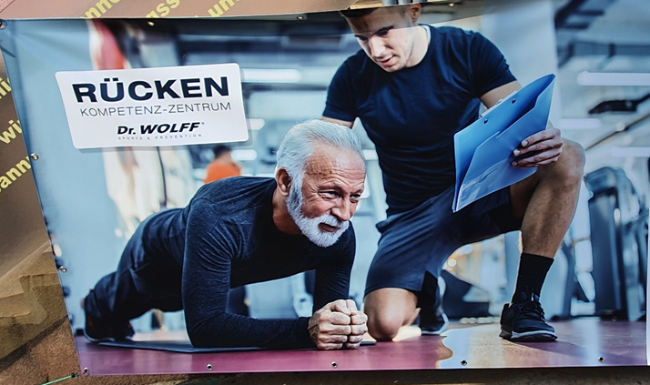 Bild eines aufgehängten Werbeplakates mit einem jüngeren und einem älteren Mann in Sportbekleidung und dem Titel "Rücken Kompetenzzentrum Dr. Wolff"