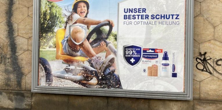 Werbeplakat für Pflaster von Hansaplast mit einem Mädchen auf einem Geländebuggy